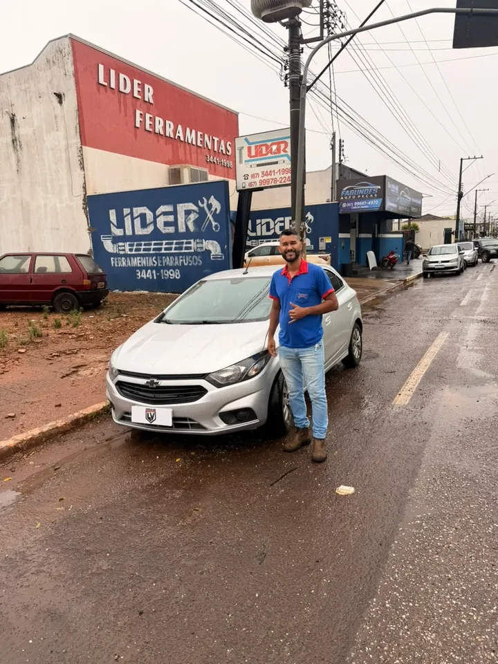 Cliente sorrindo ao lado do hatch prata que comprou na LV, com a placa da LV Veículos